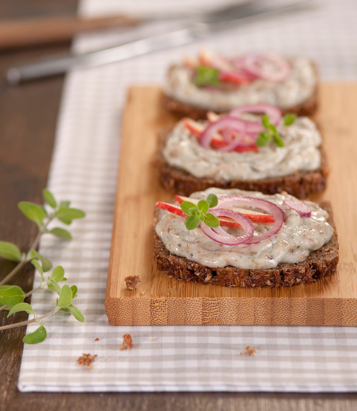 Gänsegriebenschmalz der Goosies Wurstwarenmanufaktur, dekoriert mit drei bestrichenen Scheiben Brot mit Zwiebeln auf einem Brettchen